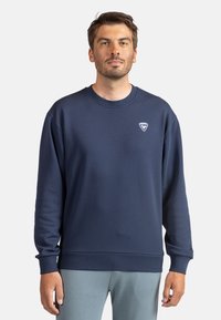 Felpa blu navy in tessuto morbido, con collo rotondo, polsini e orlo a coste, e piccolo logo sulla parte sinistra del petto.