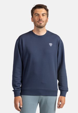Sudadera azul marino de un tejido suave, con cuello redondo, puños y dobladillo acanalados, y pequeño logo en la zona del pecho izquierdo.