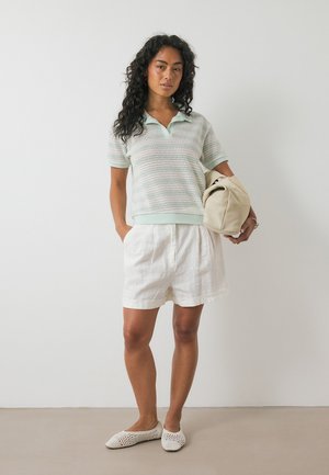 Ljusgrön kortärmad polo med strukturerade ränder; matchad med vita linnebyxor; håller en beige väska; öppen kragnivå; avslappnad passform.