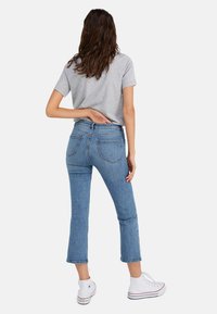 Camiseta de manga corta de color gris claro combinada con unos jeans recortados azules. Los jeans tienen una cintura alta, un leve desgastado y bolsillos traseros. Zapatillas blancas.
