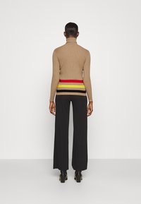 Suéter beige de cuello alto con un diseño de rayas horizontales multicolores en la cintura, combinado con pantalones de pierna ancha negros y botas de tacón.