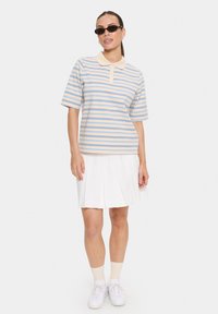 Polo à rayures beige avec des rayures bleues, à manches courtes et avec un col ; associé à une jupe plissée blanche et des baskets blanches.
