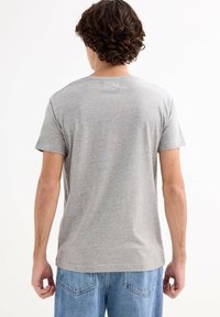 Camiseta de algodón gris con mangas cortas, cuello redondo estándar y textura suave, combinada con unos pantalones vaqueros de mezclilla azul claro.