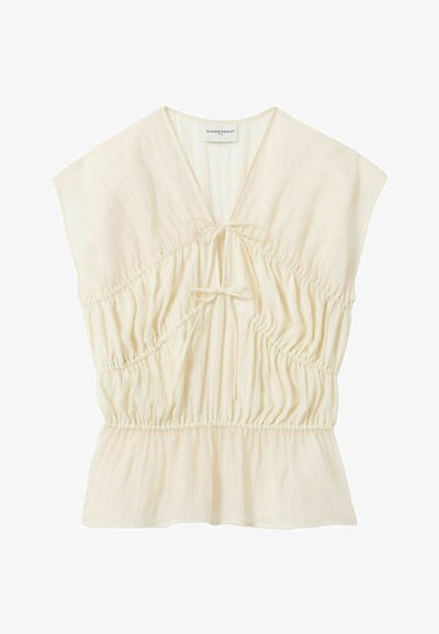Blusa leggera color crema con maniche corte a cappuccio, scollo a V, due chiusure frontali con laccetti, vita arricciata e orlo leggermente svasato.