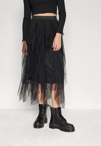 Černá vrstvená tylová sukně s elastickým pasem, doplněná černými šněrovacími botami se žlutým prošíváním a masivní podrážkou.