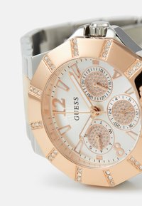 Roségold- und Silberuhr mit einem strukturierten weißen Zifferblatt, drei kleinen Ziffernblättern, Kristallakzenten und einer massiven achteckigen Lünette. Silbernes Armband.