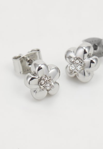 Sidabro gėlės formos auskarai su centriniu nedidelių skaidrių kristalų žiedu ir lygia, blizgia tekstūra. Užsegami užsegimais.