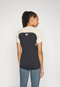 Kortærmet atletisk top i sort og beige, med et logo på ryggen, lyserøde detaljer og en tætsiddende pasform. Glat, letvægts materiale.