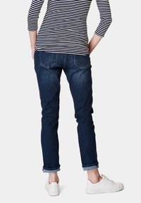 Mörk denimjeans med slim fit, uppvikta vid anklarna, i kombination med en randig långärmad topp, sedd bakifrån. Vita sneakers.