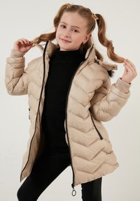 Beige pufferjakke med chevronmønster, sort lynlås, høj krave og elastiske manchetter. Quiltet design med en let blank struktur.