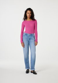 Roze geribbelde langemouwtop, hoog-gewicht lichtblauwe denim jeans, zwarte instappers met gouden accenten, effen achtergrond.
