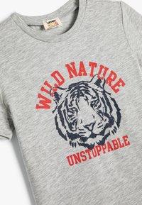 Grå bomulds t-shirt med et tiger grafik i marineblå, med rød tekst der lyder "VILD NATUR USTOPPELIG" under designet.