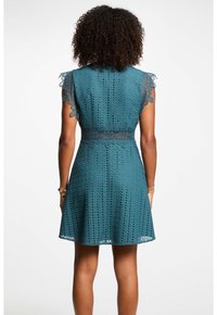 Türkises Spitzenkleid mit kurzen Ärmeln, rundem Ausschnitt und taillierter Passform. Durchgehendes Ausschnittmuster, ausgestelltete Rock und gewellte Ärmelsäume.