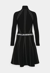 Robe en tricot noire à manches longues avec des lignes verticales blanches à pois et une taille cintrée portant le texte "KARL LAGERFELD" en blanc.