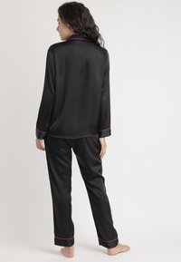 Conjunto de pijama de seda negra con parte superior de manga larga y pantalones a juego. Presenta un ribete rosa en el cuello y los puños. Textura suave y brillante.