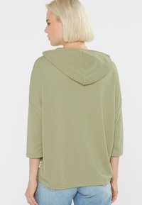 Light green, ribbed hoodie with three-quarter sleeves and a back view, featuring a large hood and relaxed fit. Minimalist design detail at hem.