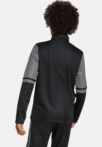Schwarze und graue Sportjacke mit hohem Kragen, langen Ärmeln und kontrastierenden Streifen an den Ärmeln. Glatte Textur, funktionales Design.
