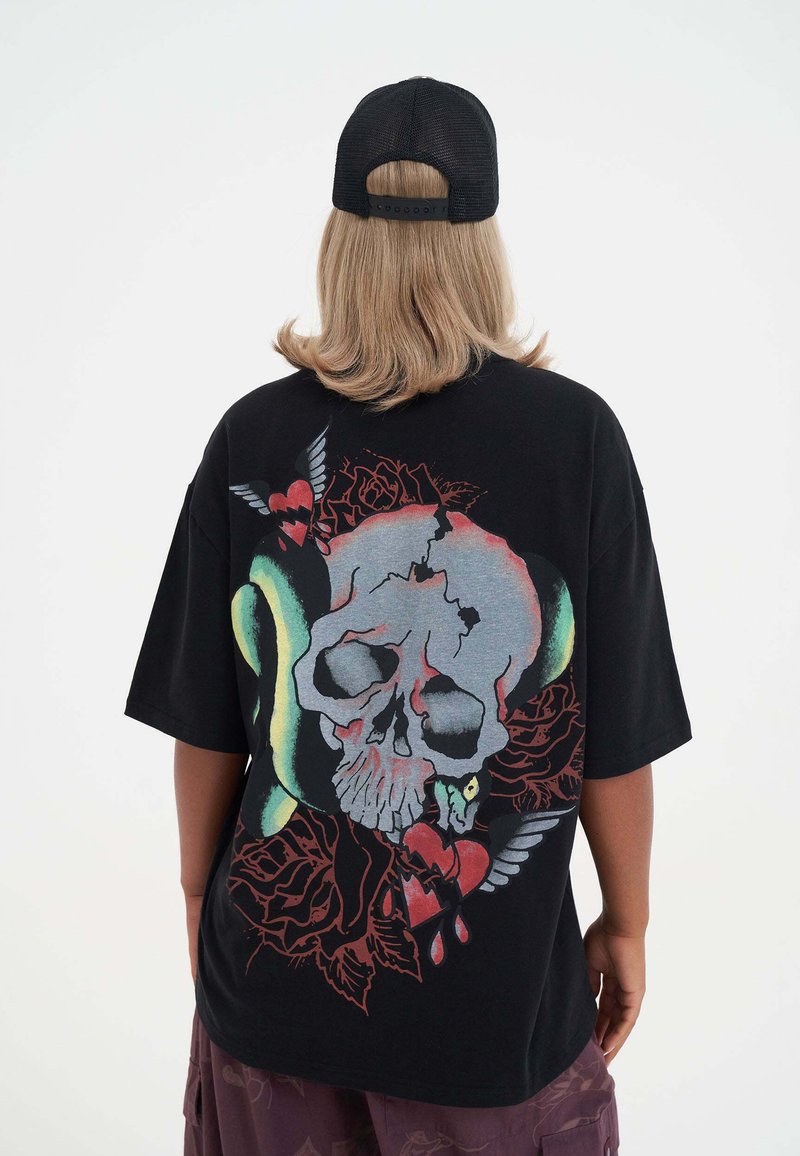 Sort oversized t-shirt med et stort, farverigt kranie grafik prydet med roser, slange og hjerter. Blød tekstur og korte ærmer.