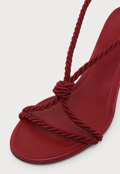 Sandale rouge avec brides en corde torsadée croisant sur les orteils et le pied, détail nœud au centre et semelle intérieure en cuir lisse.