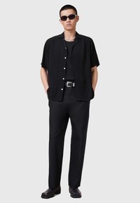 Schwarze kurzärmlige Knopfhemd mit strukturiertem Muster, kombiniert mit schwarzen Hosen und passenden Schuhen. Accessoires umfassen dunkle Sonnenbrillen.