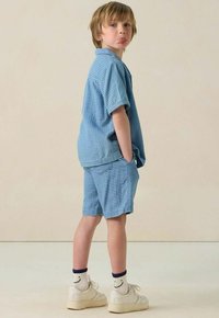 Hellblau gestreiftes Poloshirt mit kurzen Ärmeln und passender Shorts. Weiße Sneakers mit Socken mit Smiley-Gesicht. Schlichtes Design, lässige Passform, weicher Stoff.