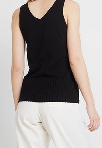 Black sleeveless top with a V-neck, featuring ribbed texture at the bottom hem. The fabric appears soft and fitted.