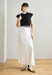 Black capped-sleeve top paired with a white maxi skirt, accented by a studded black belt and silver heeled ankle boots.
