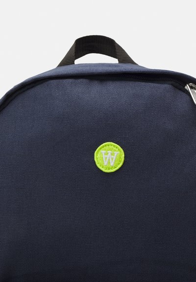Geantă din canvas bleu marin, cu un logo brodat rotund, verde și alb pe față, având un mâner superior și închidere cu fermoar.