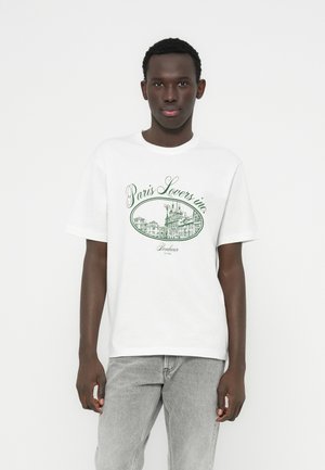 T-shirt en coton blanc avec un imprimé graphique vert représentant des bâtiments parisiens et les textes "Paris Lovers inc." et "Bontéur Est. 2022."