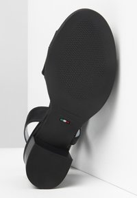 Sandalo nero con suola piatta, caratterizzato da cinturini in pelle liscia e suola in gomma testurizzata. Include marchio e indicazioni della taglia.