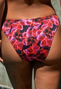 Virágos bikini alsó élénk piros és lila orchidea mintával, fekete háttérrel, finom márkázással. Sima textúra.