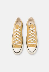 Gule lerrets-sneakers med hvite snører, gummitopper og svarte sideakenter. Har detaljer med søm og et flatt såledesign.