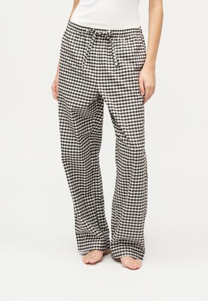 Personne portant un pantalon ample à petits carreaux noirs et blancs avec une taille à cordon, un haut blanc et les pieds nus.
