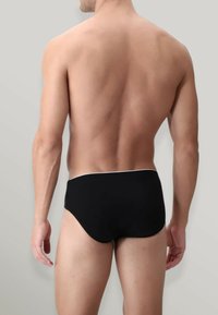 Slip da bagno neri con una cintura bianca a contrasto, caratterizzati da una superficie liscia e un design aderente, mostrati dal retro su uno sfondo neutro.