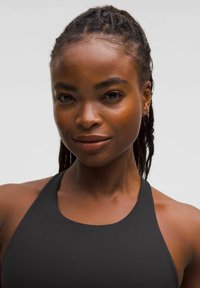 Crni atletski halter top, glatka tkanina, uski kroj, široke naramenice i minimalistički stil. Boja kože i neutralna pozadina.