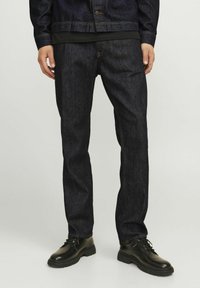 Jeans de denim oscuro con corte recto, con pespuntes naranjas, cremallera y combinados con botas negras de cordones. Textura suave.