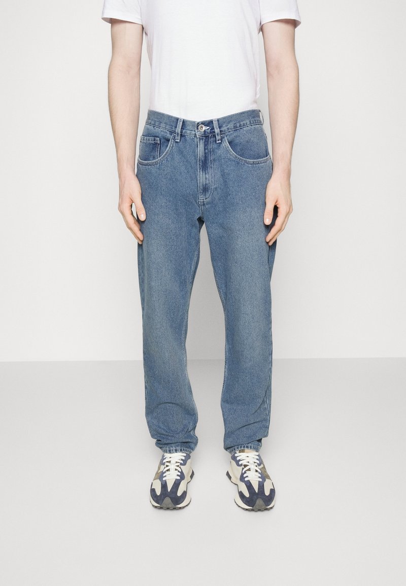 Jeans in denim azzurro chiaro con una vestibilità rilassata, dotati di tasche frontali, passanti per la cintura e cuciture a vista. Abbinati a sneakers multi-colorate.
