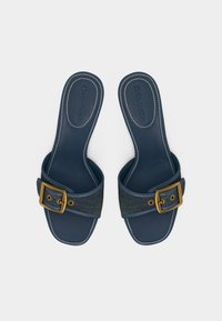 Ζευγάρι σαγιονάρες σε σκούρο μπλε χρώμα με φαρδιές τιράντες από denim, που διαθέτουν μεγάλα χρυσά μεταλλικά πόρπες και εμφανείς λευκές ραφές.