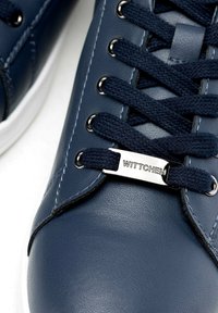 Sneaker in pelle sintetica blu navy con cuciture orizzontali, lacci tondi e un'etichetta di marca in metallo con la dicitura "WITTCHEN". Suola in gomma bianca.
