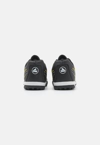 Zapatillas deportivas negras con líneas de acento amarillas, parte superior texturizada y suela de goma. Presenta un logo circular en el talón.