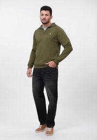 Oliivinvihreä hupullinen collegepaita neljännesvetoketjulla ja etutaskulla, yhdistetty tummiin farkkuihin ja beigeihin tennareihin. Yksinkertainen muotoilu ilman kuvioita.