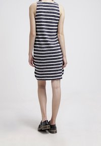 Niebiesko-biały w poziome paski bezrękawnik z dopasowanym krojem, wykonany z teksturowanej tkaniny. Noszony z czarnymi butami o płaskiej podeszwie.