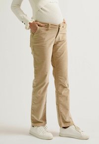 Beige Cordhosen mit bequemem Schnitt, ausgestattet mit Seitentaschen und feiner Rippstruktur, kombiniert mit weißen Sneakern.