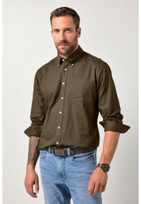 Braunes Hemd mit Knopfleiste, Brusttasche, hochgekrempelten Ärmeln und weißen Knöpfen. Getragen mit hellblauen Jeans und einem braunen Gürtel.