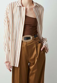 Lightweight, striped blouse in cream and rust, paired with a brown tank top and high-waisted, tan satin trousers featuring pleats and a belt.