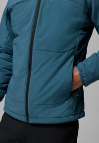 Türkise isolierte Jacke mit durchgehendem Reißverschluss, seitlichem Taschenfach und elastischen Bündchen. Glattes Material mit matter Oberfläche.