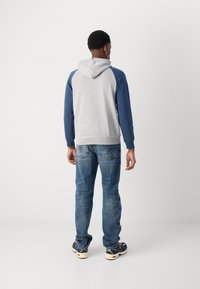 Sudadera gris con mangas azules, con capucha ajustable y dobladillo acanalado. Usada con jeans azules y zapatillas multicolores.