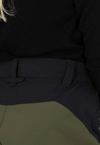 Oliwkowe spodnie z czarnym elastycznym paskiem w talii, cechujące się gładką fakturą oraz boczną kieszenią z ozdobnym, złożonym brzegiem.