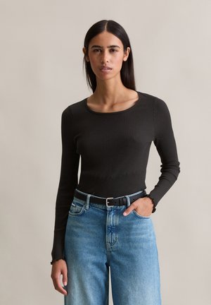 Zwarte geribbelde longsleeve top met een brede halslijn, gecombineerd met lichtblauwe high-waisted jeans en een zwarte riem. Eenvoudig en aansluitend ontwerp.