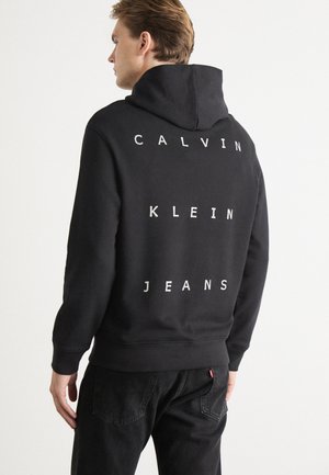 Black hoodie made of cotton with a kangaroo pocket, featuring white block letters spelling "CALVIN KLEIN JEANS" on the back.
